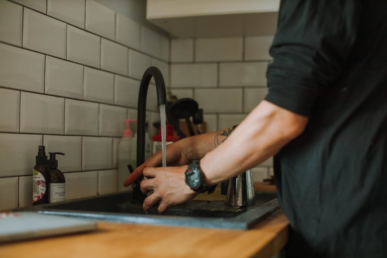 Close-up of a person washing hands at a sink with running water, wearing a wristwatch.