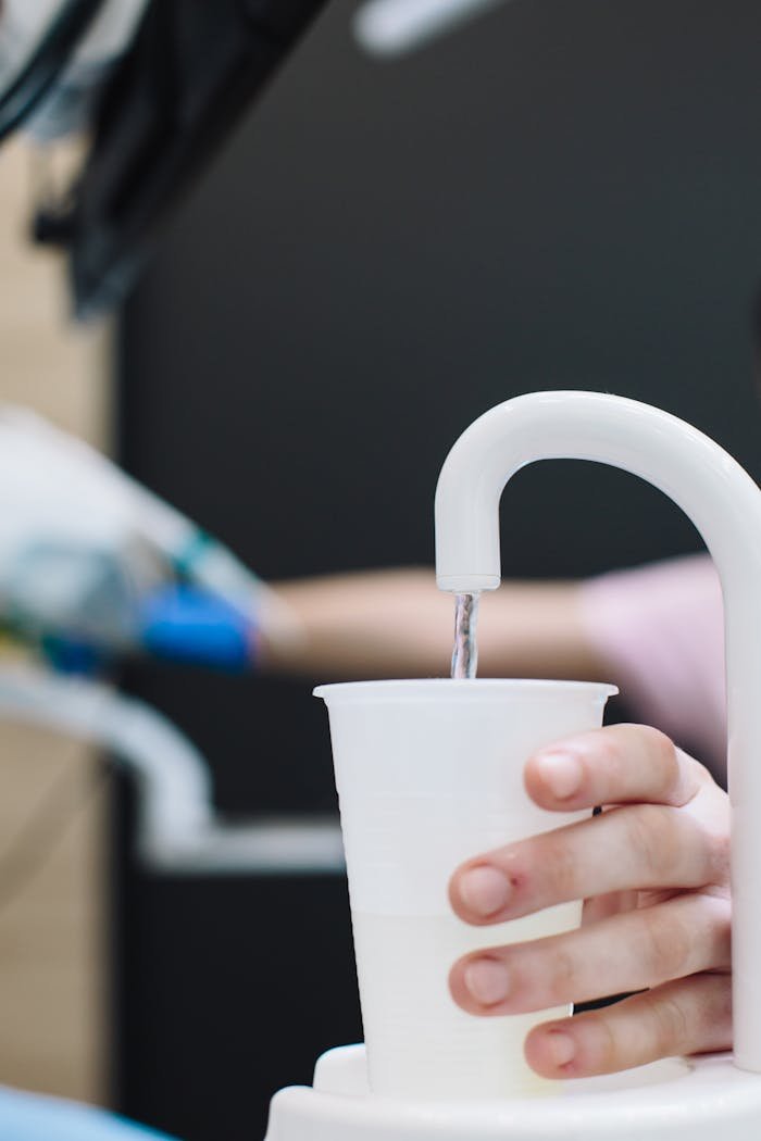 A person filling a water cup from a dental office water dispenser.